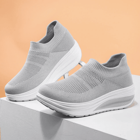 Grey casual women's sneakers on a white platform, featuring a breathable knit design and comfortable sole.